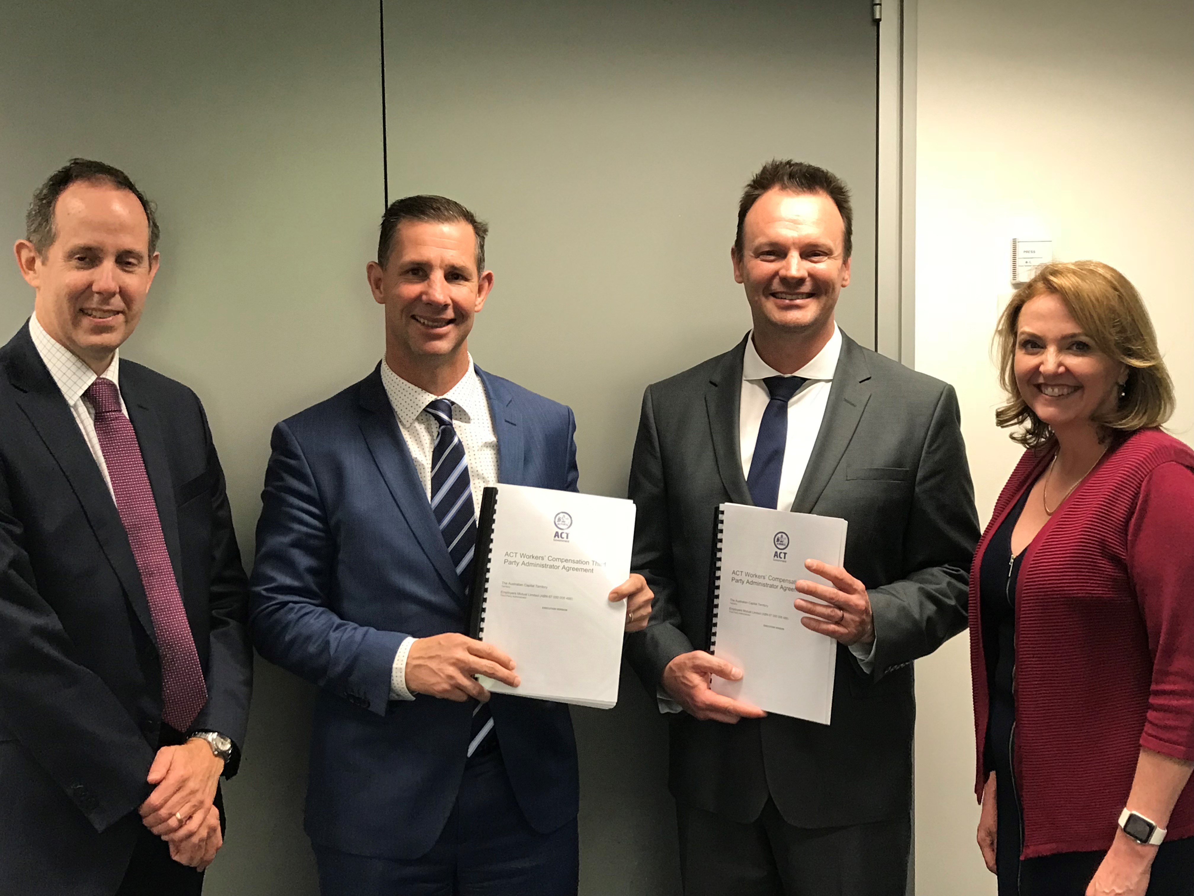 Four people holding agreements in suits, smiling.