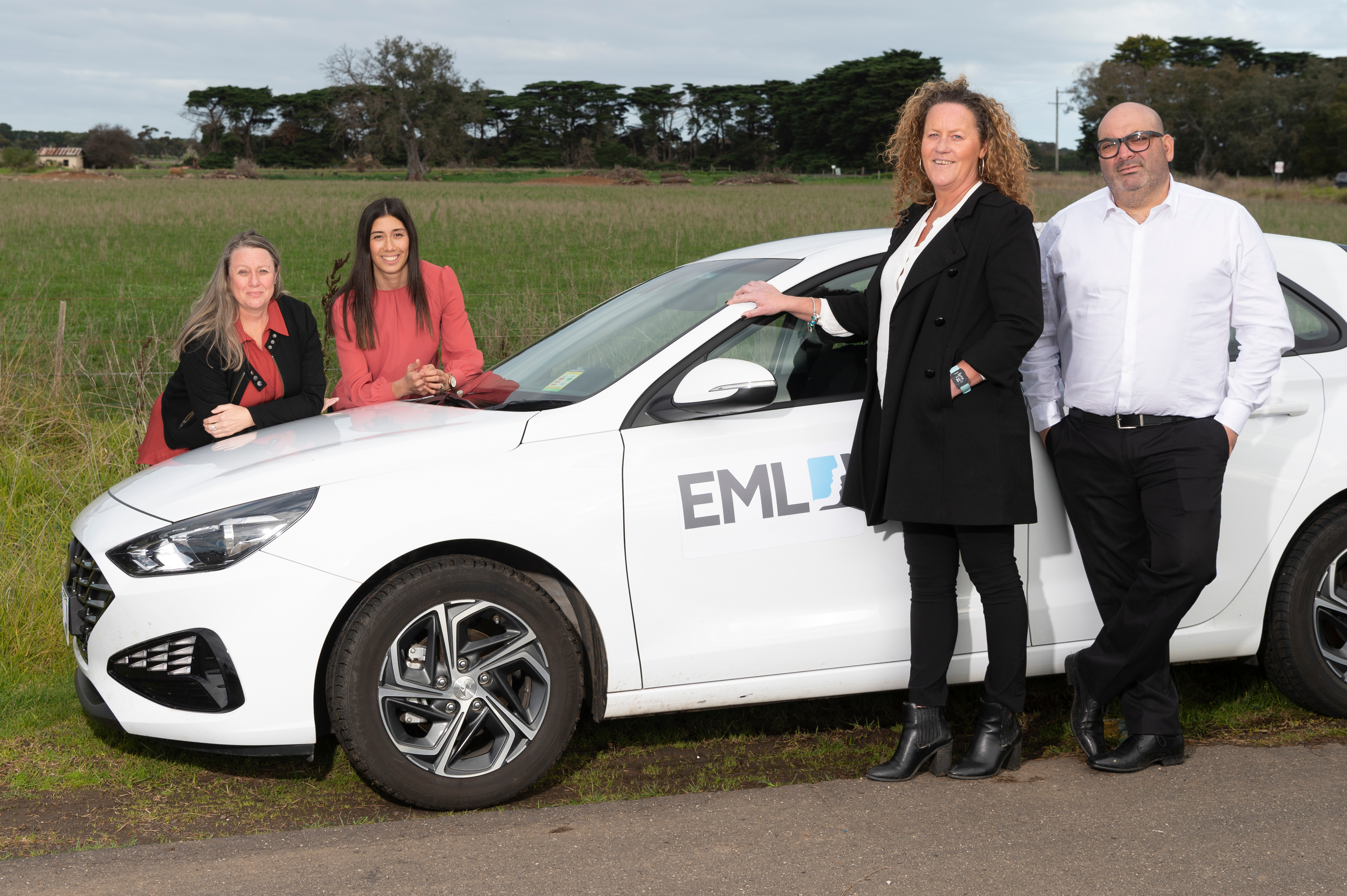 Four people posing with a white car outdoors.