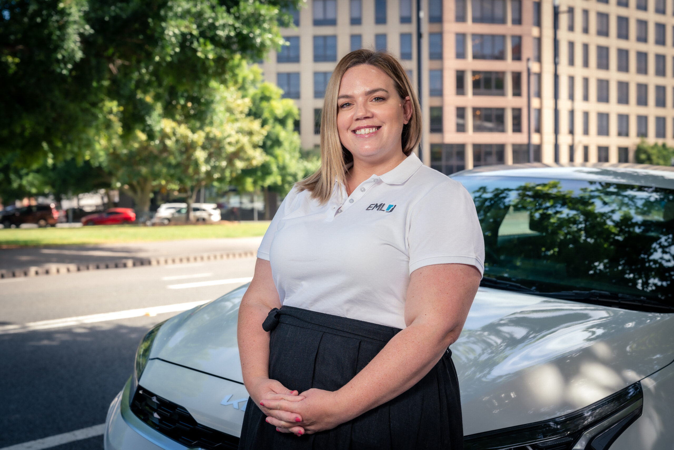 Smiling woman standing beside a white car.
