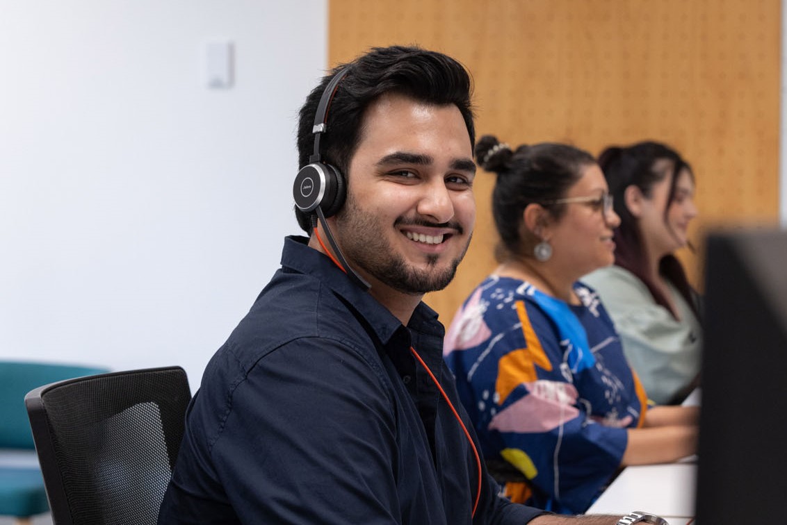Person smiling, wearing headphones at a computer.