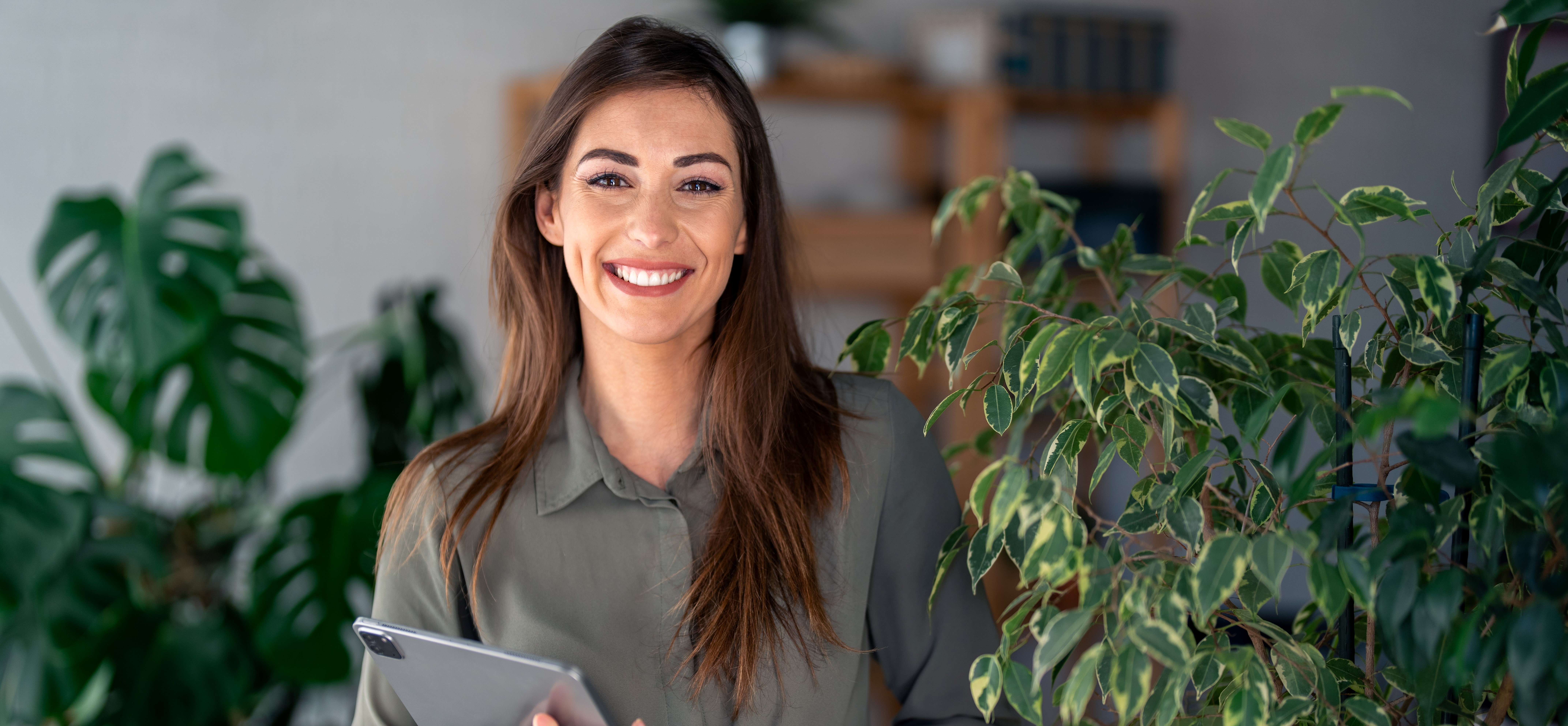 Smiling woman holding tablet, standing by plants.