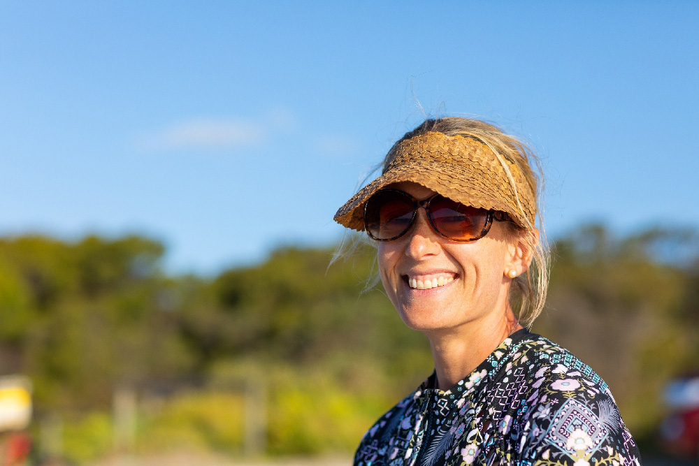 Smiling woman outdoors wearing sunglasses and hat.