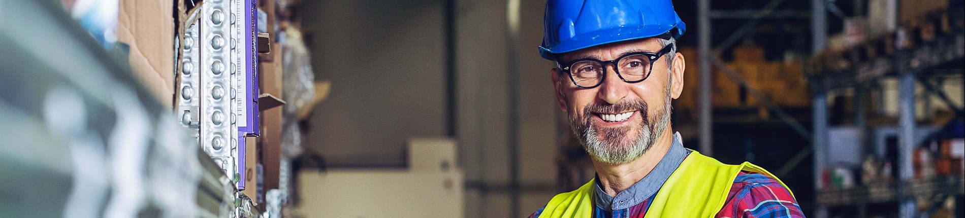 Smiling warehouse worker in hard hat and safety vest.