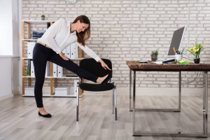 Woman stretching leg near an office chair.