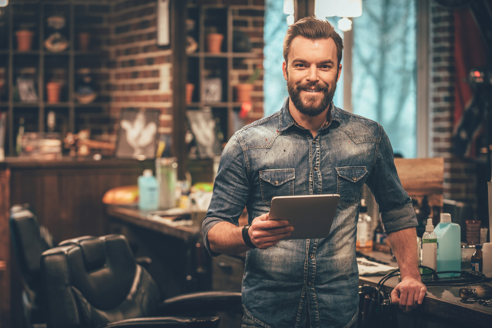 Smiling barber holding a tablet in salon.