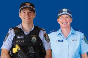 Two police officers smiling against blue background.